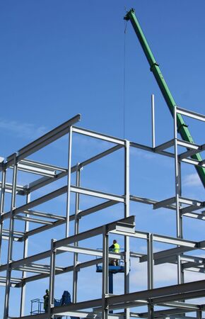 Cherry picker and crane beside metal frame of new building