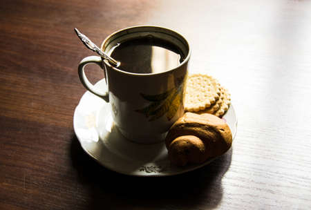 Cup of coffee on a plate in soviet style with pastry on brown tableの写真素材