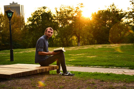 Guy sitting on a bench in the park reading bookの写真素材