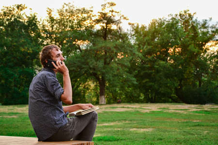 Guy with book talking on the phone in parkの写真素材