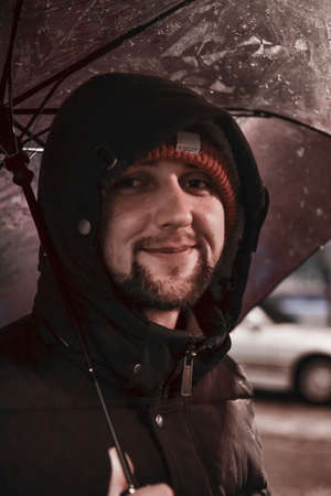 Young happy man under umbrella looking at camera smiling. Bad weatherの写真素材