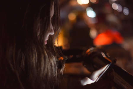 Girl using smart phone at night in front of blurred city lightsの写真素材