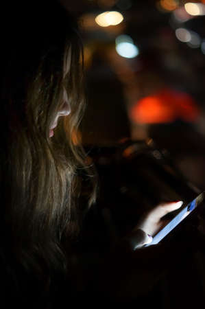 Girl using smart phone at night in front of blurred city lightsの写真素材