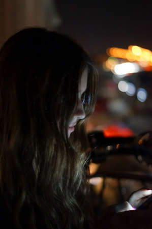 Girl using smart phone at night in front of blurred city lightsの写真素材