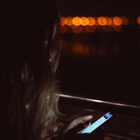 Girl using smart phone at night in front of blurred city lightsの写真素材