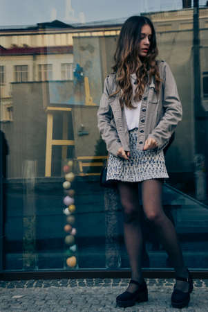 Stylish girl in skirt standing near glass shop window on city streetの写真素材