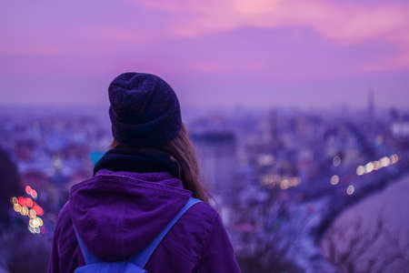 Girl looking at winter evening cityscape, purple violet sky and blurred city lightsの写真素材