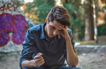 Worried teenage boy sitting holding head thinking how to solve problemsの写真素材