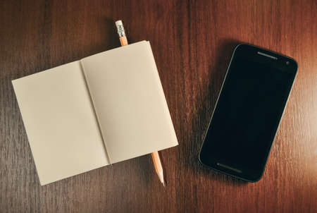 Open pocket book, pencil and mobile smart phone on wooden table, top viewの写真素材