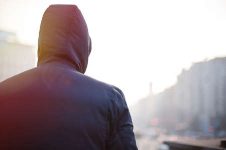 Lonely hipster man in hood walking on city street in the eveningの写真素材