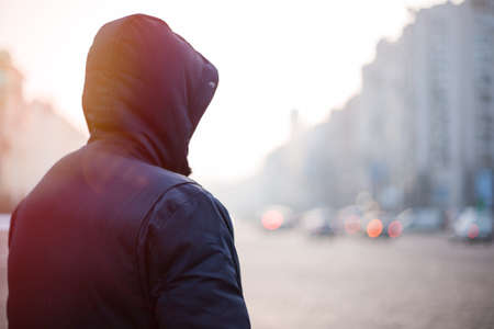 Hipster man in hood walking on city street in the eveningの写真素材