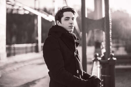 Portrait of a thoughtful hipster guy standing on the bridge. Film sepia effect with grainの写真素材