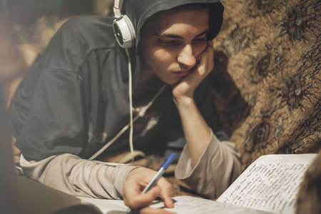 Teenage student guy studying lying on the sofa at home listening to musicの写真素材