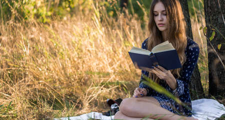 Girl sitting under a tree reading book in summer forestの写真素材