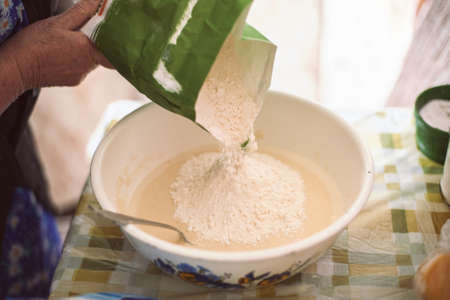 Grandmother pouring flour into pancake batterの写真素材