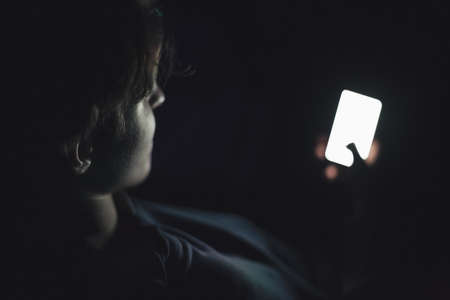 Teenage boy using smart phone in the darkの写真素材