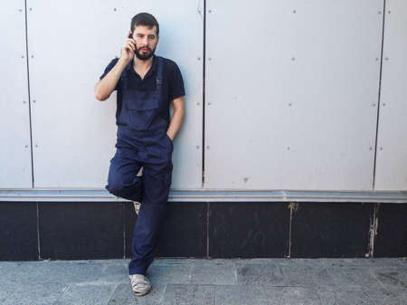 Worker on a break talking on mobile phone standing near the wall