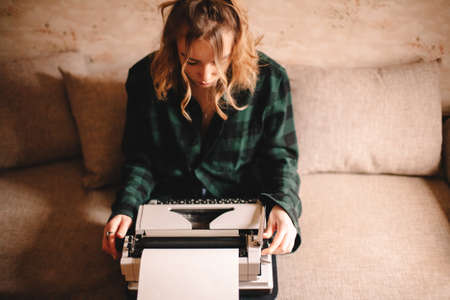Young female writer using typewriter while sitting on sofa at homeの写真素材
