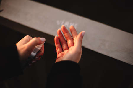 Cropped image of young woman applying hand sanitizer antiseptic while disinfecting hands standing outdoors by railing in cityの写真素材