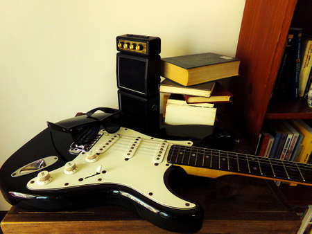 An electric guitar on the table surrounded by books and a booster.