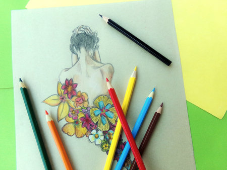 Coloring pencils on paper sheet with a woman's drawing and flowers.