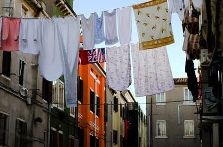 A lot of clothes, sheets and underwear streched between of the housesの写真素材