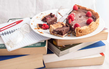 Sliced and crumbled chocolate cake and raspberries on top of a stack of books during the studyの写真素材