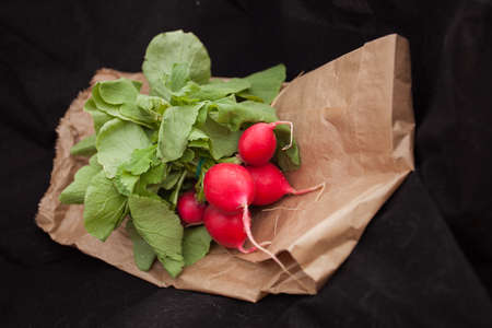 Raw radishes with leaves on paper bag and black background.の写真素材