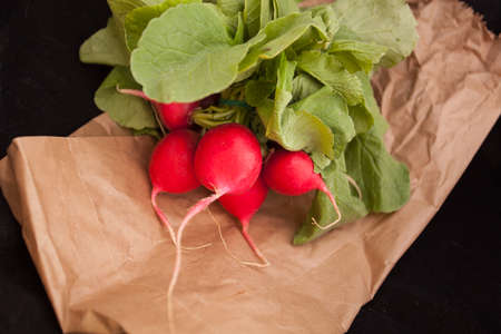 Raw radishes with leaves on paper bag and black background.の写真素材