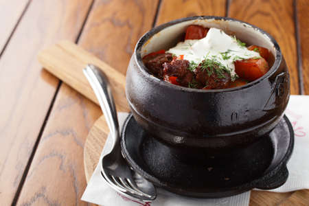 black pot on wooden tabe with hot meat and tomatoの写真素材