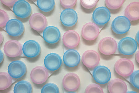 Containers for storing contact lenses. The lids are pink and blue.