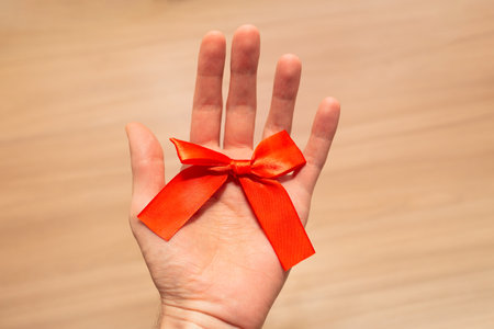 Red bow in hand on wooden background.の写真素材