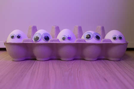 Eggs with eyes. Backlit background. A box with white eggs.