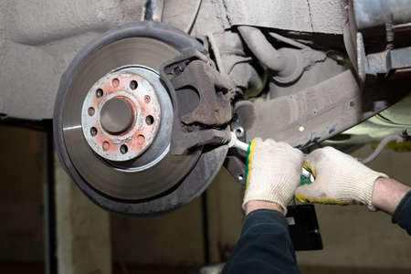 A man working in a car service. Replace brake disc and pads. A young mechanic is repairing the disc...