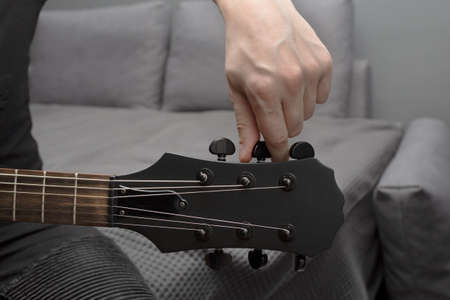 Black electric guitar tuning. Fingers are turning the tuning peg. Hand in the frame. Learning to play the guitar.の写真素材