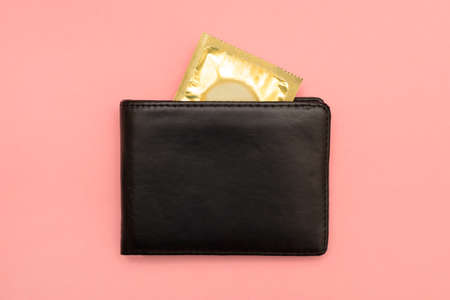 Condom in a wallet on a pink background. Bladeless sex. Save your health. Condom in gold packaging.の写真素材