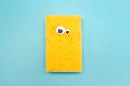 Yellow cleaning sponge with googly eyes. A funny face. Round eyes. Blue background. Holiday.の写真素材