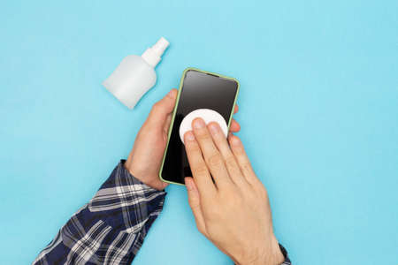 A man in a shirt disinfects his phone and wipes it with a cotton pad treated with an antiseptic.