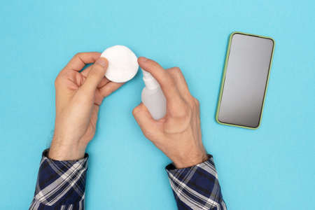 A man puffs an antiseptic on a cotton pad to disinfect his phone. Virus protection. Taking care of your health.の写真素材
