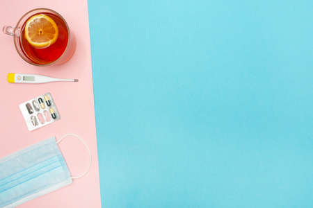 Catch a cold. Flu season. Disease. Flat lay. Medical mask, pills, thermometer, and lemon tea. Place for your text. Copy space. Mockup. Advertising. Pink and blue background.の写真素材
