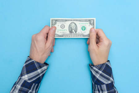 Man holds two dollars on a blue background. Financial literacy. Bankrupt. Money is tight. Importance of savings.の写真素材