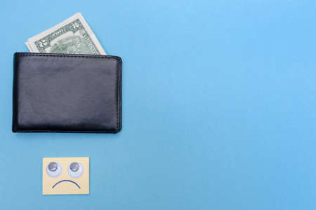 Two dollars are in the wallet. Place for your text. Copy space. Sad smiley looks at the wallet. Blue...