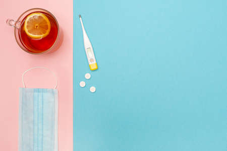 Catch a cold. Flu season. Disease. Flat lay. Medical mask, pills, thermometer, and lemon tea. Place...