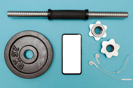 Dumbbells, mobile phone with white screen and headphones on a blue background. Mockup. Copy space. Sports and Fitness background. Flat lay. Health care. Vertical.の写真素材