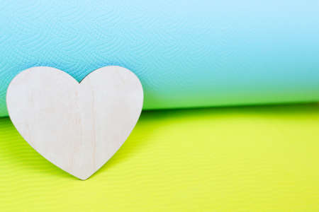 Blue and yellow yoga mat and wooden heart. Love concept for yoga, pilates and fitness. Place for text and logo. Copy space.の写真素材