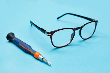Glasses for vision and a screwdriver for repairs on a blue background. Glass repair concept. workshop.の写真素材