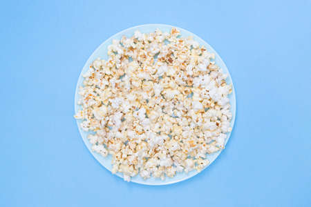 Popcorn on a turquoise plate for watching a movie. Blue background. Copy space. Flat lay. Top view. Quick and tasty snackの写真素材