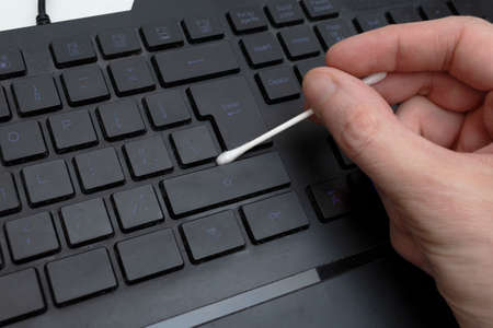 Man cleaning a dirty keyboard with a cotton swab
