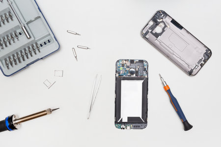 Disassembled broken phone, accessories, and tools to repair it. White background. Service center for smartphones. Phone repair concept. Flat lay. Top view.の写真素材