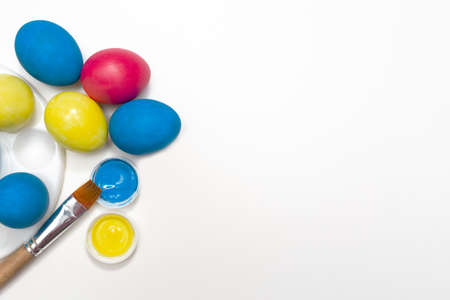 Easter holiday. The process of painting an egg on a white background. Paint, brush and water. copyspace. Place for text. flat lay. top view. holiday preparation concept.の写真素材